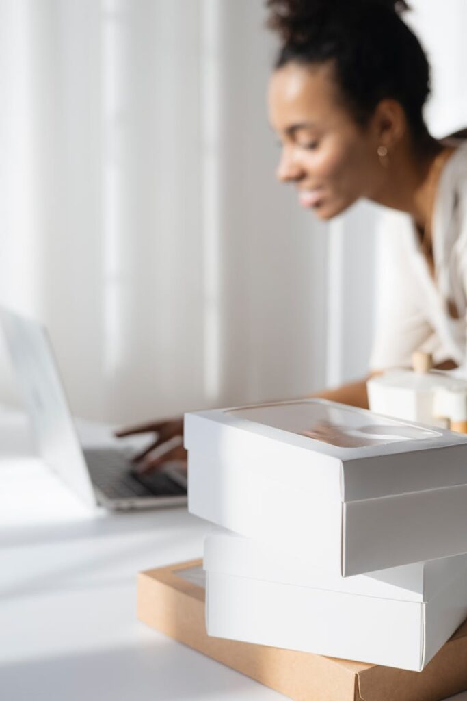 A focused woman planning her bakery business with a laptop and packaging boxes.